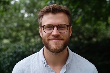 Fototapeta premium Young man with glasses smiling outdoors in a natural setting surrounded by greenery