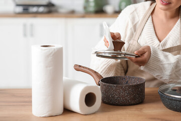 Beautiful young happy woman wiping pots with paper towels in kitchen, closeup