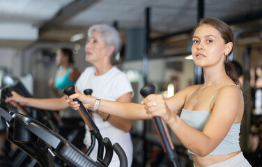 Fototapeta premium Slender athletic girl during cardio exercises on elliptical simulator in fitness center. Sports to max. Electronic tracking for most productive workout