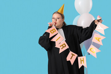 Young happy female judge in party hat with birthday cupcake, garland and balloons blowing whistle on blue background