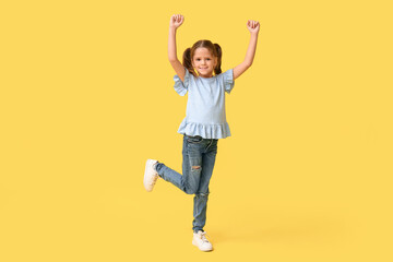 Happy little girl celebrating success on yellow background