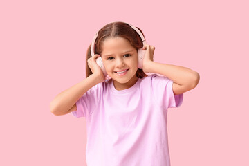 Happy little girl in headphones listening to music on pink background