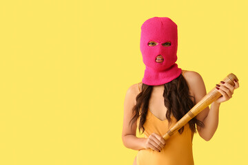 Stylish young Asian woman in pink balaclava with baseball bat on yellow background