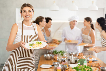 Young girl visiting culinary school holds plate with cooked chicken fillet in hands, successful result of studies