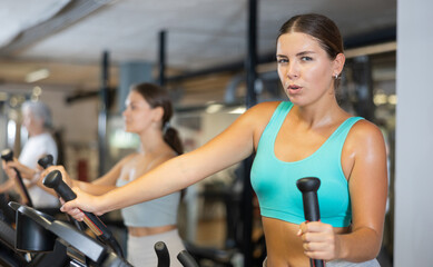 Active athlete young woman engaged in intensive high interval training on ellipsoid simulator....
