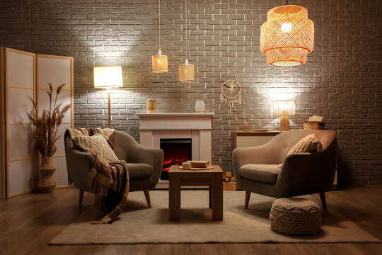 Interior of stylish cozy living room with fireplace, armchairs and glowing lamps in evening