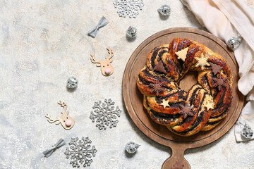 Wooden board with tasty Christmas pastry wreath, decor and cookies on light grunge background