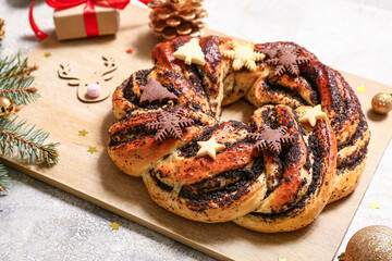 Wooden board with tasty Christmas pastry wreath, fir tree branches, decor and cookies on light grunge background