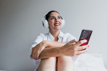 latin adult woman resting on bed using mobile phone and headphones at home in Mexico Latin America, hispanic middle aged female