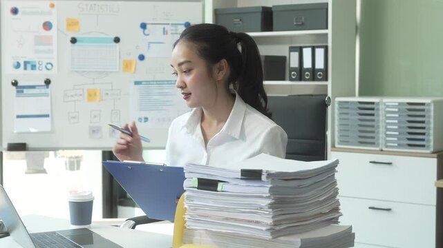 A young Asian businesswoman works alone at a desk with a laptop, stack of papers, tablet, and mobile phone. She looks happy and inspired, managing appointments and analyzing equity financing.