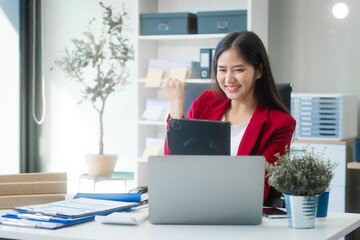 A young Asian woman works diligently at her desk in a bright office room during the day. Surrounded...