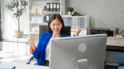 A young Asian woman works at her desk in an office room, managing time with a laptop, papers, and...