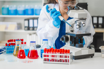 A young Asian woman works in a laboratory, conducting chemical and blood tests. Wearing goggles,...