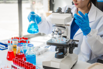 A young Asian woman works in a laboratory, conducting chemical and blood tests. Wearing goggles,...