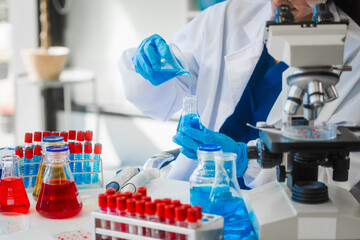 A young Asian woman works in a laboratory, conducting chemical and blood tests. Wearing goggles,...