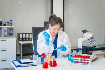 A young Asian woman works in a laboratory, conducting chemical and blood tests. Wearing goggles,...