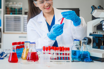 A young Asian woman works in a laboratory, conducting chemical and blood tests. Wearing goggles,...