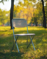 A simple folding chair placed on grass in a sunlit park setting.