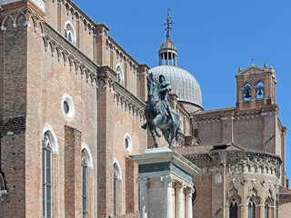 Statue of Bartolomeo Colleoni and church of Santi Giovanni e Paolo with dome and bell tower on a summer day with clear blue sky in Venice, Italy