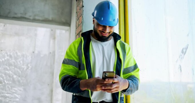 Man, engineer and typing with phone for construction, planning project or check building schedule. Happy architect, mobile and builder at site for communication, text and infrastructure maintenance