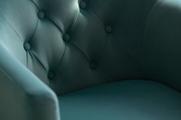 Close-up of a soft blue velour armchair with carriage upholstery in the shadows and rays of the sun with copy space.