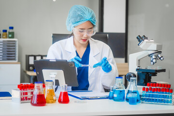 A young Asian woman works in a laboratory, conducting chemical and blood tests. Wearing goggles,...