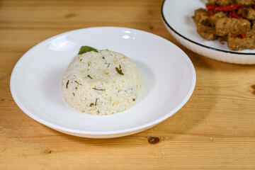 Lime leaf rice on wooden table. Fried onion on top. thisi is Indonesian cuisine on rattan plate. Nasi daun jeruk