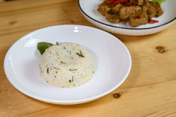 Lime leaf rice on wooden table. Fried onion on top. thisi is Indonesian cuisine on rattan plate. Nasi daun jeruk