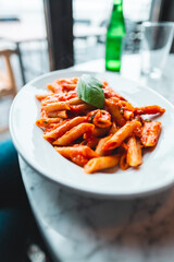 Delicious Italian Penne Pasta Dish Served on a White Plate with Fresh Basil Garnish in a Cozy Restaurant Setting Featuring Natural Light