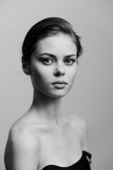 Fototapeta premium Elegant black and white portrait of a beautiful young woman with a neutral expression, showcasing simple fashion and natural beauty. Beauty and minimalism concept.