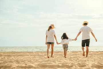 Happy Asian parents with their daughters enjoying playful at beach. Little girls with their mother and father holding hand of child walking on sand beach. Positive family outdoor activity