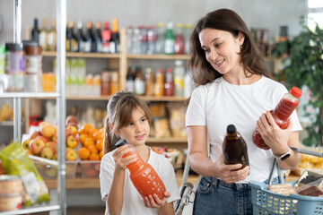 While shopping in grocery store, girl with aunt family buyers choosing juice. They look package of...