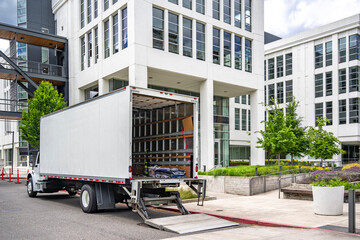 Relocation specialist on middle rig semi truck with box trailer with open back door and lift making...
