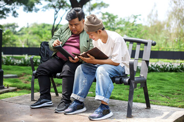 Two Men College Student Sitting on Bench Doing Homework Outdoors Together 