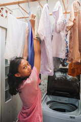 Asian teenage girl doing laundry for domestic chore at home looking happy smiling