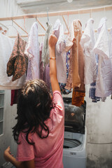 Asian teenage girl hanging clothes to dry while doing laundry for domestic chore at home