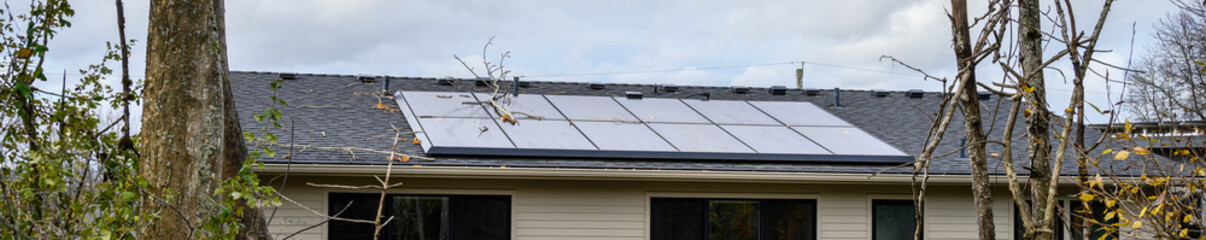 Solar panels on an asphalt shingled roof on a residential house, cloudy sky in background, green energy and power generation
