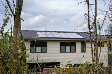 Solar panels on an asphalt shingled roof on a residential house, cloudy sky in background, green energy and power generation
