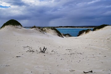Serene sandy dunes meet tranquil waters under dramatic skies near the coast