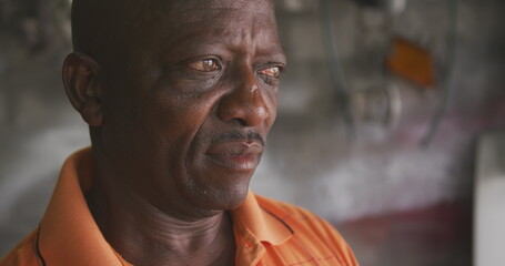 Portrait close up of an African man in a township, wearing an orange shirt and leaning ahead, slow m