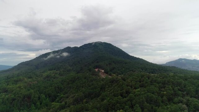 A steady aerial shot of a drone flying toward Cerro Uyuca, a biological reserve in Honduras, showing lush greenery and signs of deforestation and construction at the mountain's base.