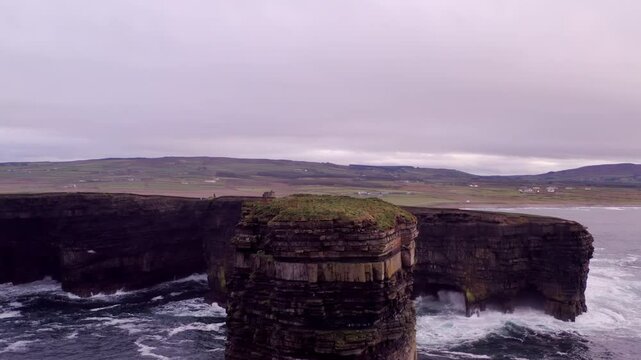 Drone approach over Dun Briste sea stack to Downpatrick Head peninsula cliffs, soaring above grasslands