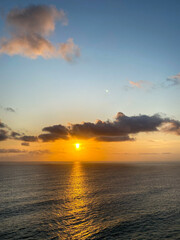 Obraz premium A sunset view over the vast ocean with golden orange sky and soft white clouds.