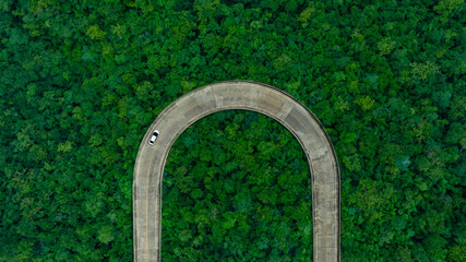 Aerial view of dark green forest road and white electric car Natural landscape and elevated roads Adventure travel and transportation and environmental protection concept