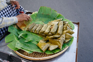 Rice cake wrapped in banana leaf. Street vendor in Cambodia. Asian traditional dish.