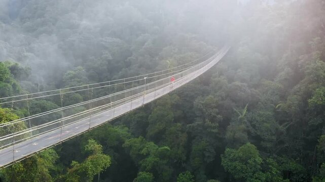 Aerial view of a beautiful wooden suspension bridge crossing a river surrounded by forests in Situ Gunung Suspension Bridge, Sukabumi, West Java.