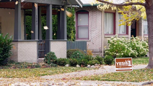 Slow Motion static shot of leaves falling in front of a historic home with a political sign in the front yard