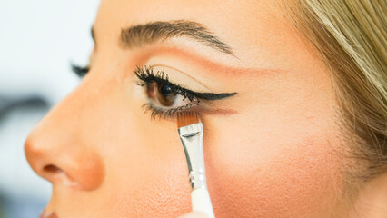 beautician applying makeup to woman's eyes