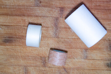 Three different size rolls of plasters in white and brown on a brown wooden background.