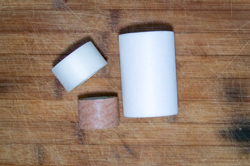 Three different size rolls of plasters in white and brown on a brown wooden background.